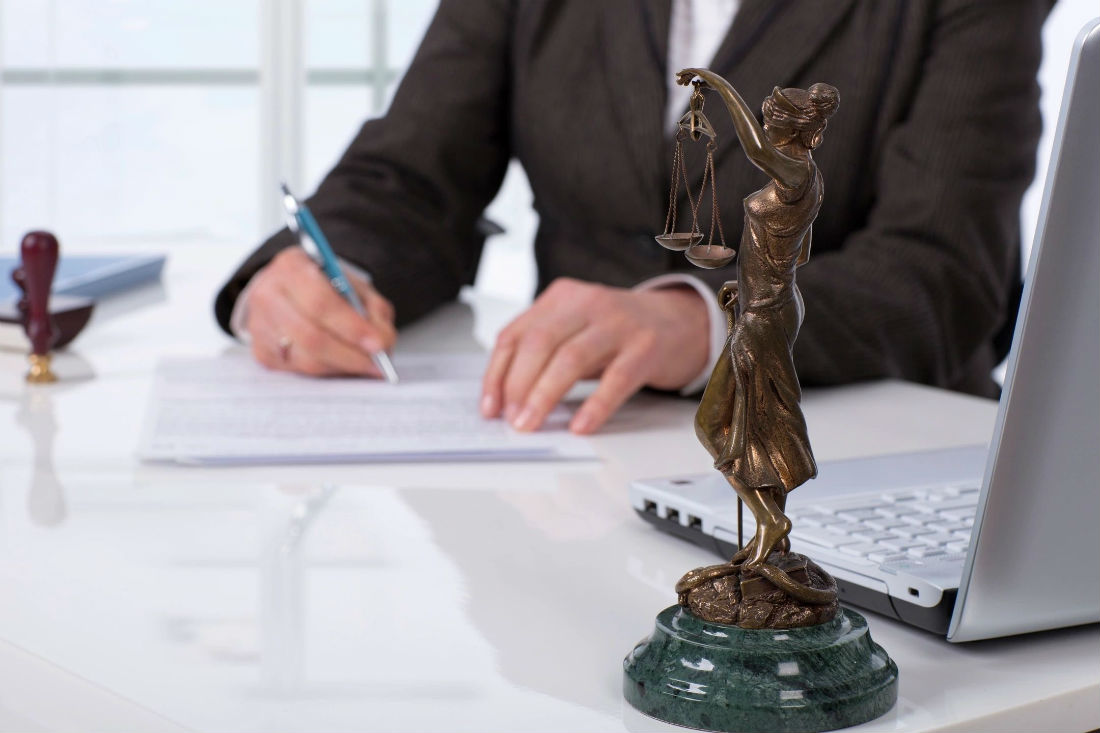 A man is writing on paper next to a statue of justice.